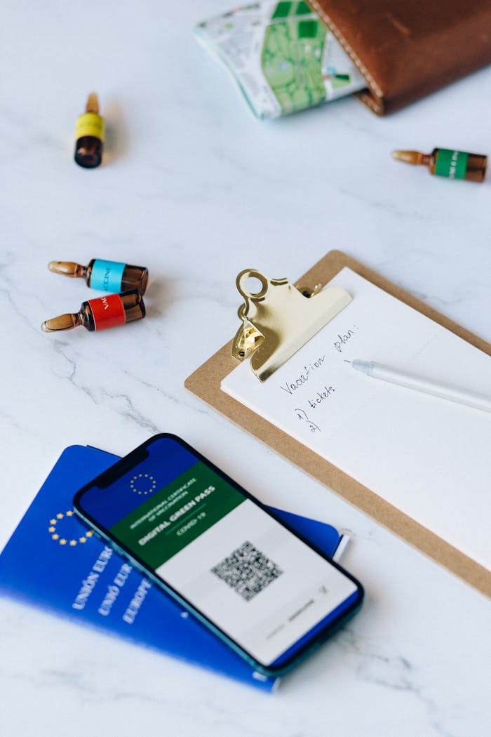 A flat lay of a smartphone showing a vaccine passport, passport, clipboard, and vaccines, symbolizing travel readiness and COVID-19 safety measures.